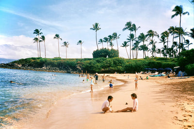 Hand holding a white and black 35mm camera against sunny blue California skies.