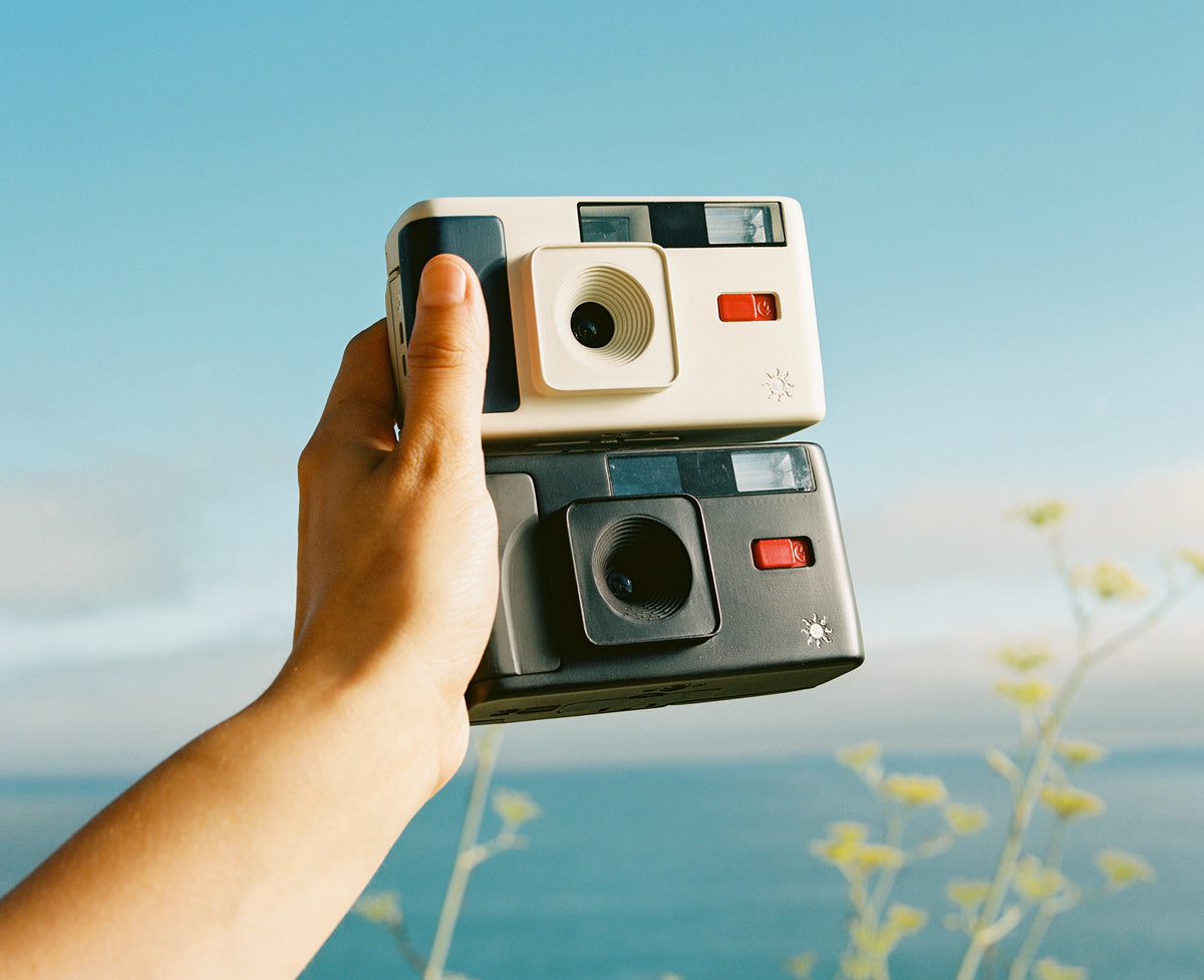 Hand holding a white and black 35mm camera against sunny blue California skies.