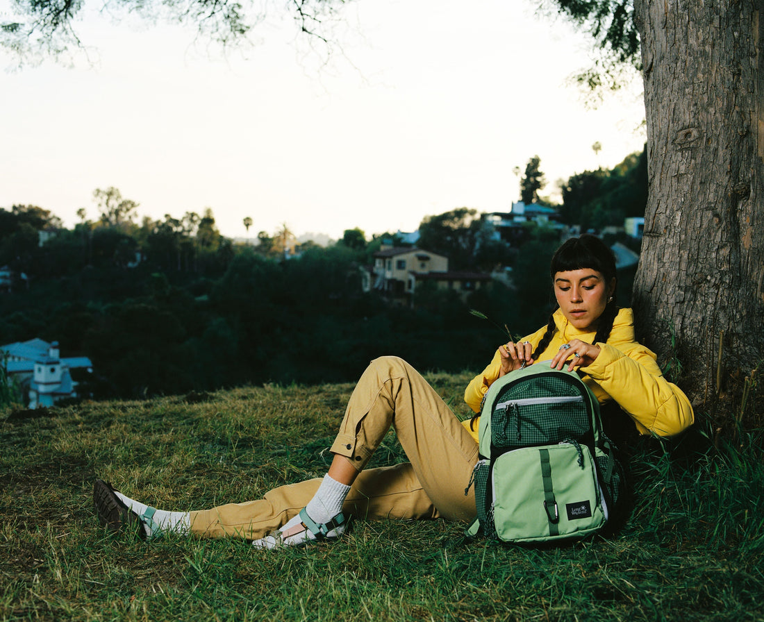 Woman sitting near a tree opening the Morro backpack to grab a film camera.